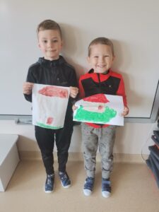 Dwóch chłopców z uśmiechem na twarzy prezentuje swoją pracę plastyczną "Mój dom". Dom namalowany farbami. 