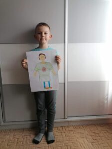 Chłopiec prezentuje swoją pracę plastyczną "Koszulka sportowca". 