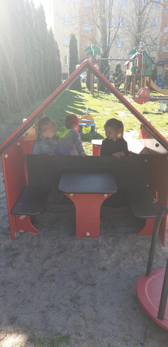Trójka dzieci siedzi w małym domku na placu zabaw w ogrodzie.  