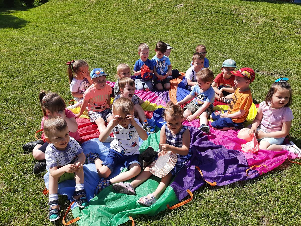 Grupa dzieci siedzi w ogrodzie na kolorowej chuście.