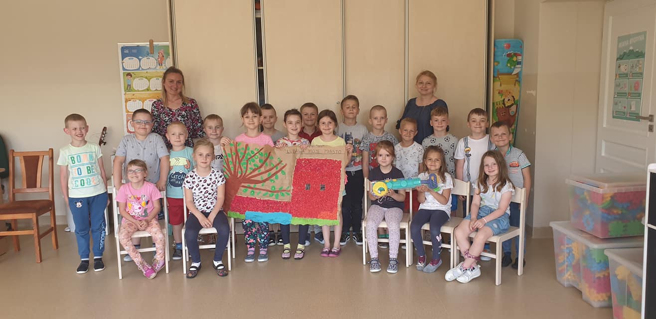 Dzieci z grupy "Tygryski" wspólnie pozują do zdjęcia trzymając pracę plastyczną, która zajęła trzecie miejsce w konkursie "Lubawa Moje Miasto". Z dziećmi pozuje Pani Dyrektor oraz organizatorka konkursu. 