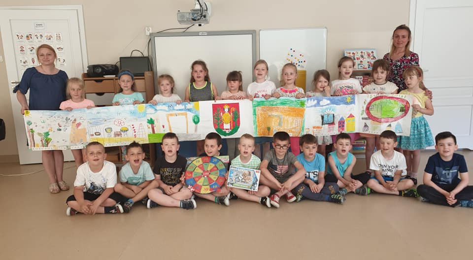Zdjęcie przedstawia dzieci z grupy "Żółwiki", które trzymają swoją pracę plastyczną, która zajęła drugie miejsce w konkursie o Lubawie. Z dziećmi pozuje Pani Dyrektor oraz organizatorka konkursu.