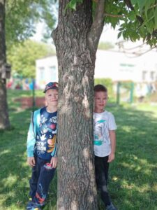 Na zdjęciu widać dwóch chłopców, którzy opierają się o pień drzewa.