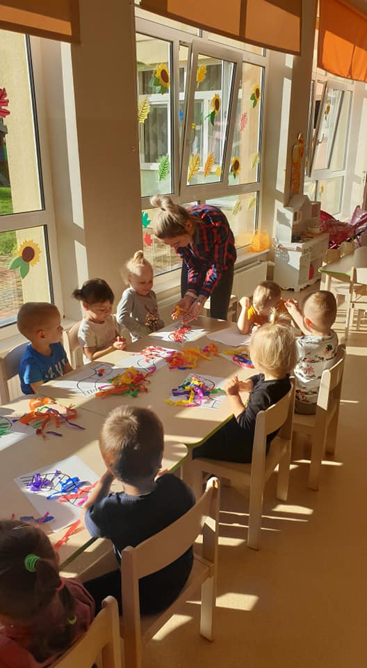 Przedszkolaki tworzą jesienny szal według własnego pomysłu. Nauczyciel podpowiada dzieciom jak ozdobić swoją pracę kawałkami kolorowej krepy.