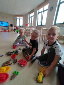 Na zdjęciu trzech chłopców, którzy bawią się małymi autami w sali przedszkolnej.