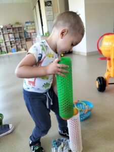 Na zdjęciu chłopiec, który przesypuje kolorowe piłeczki z plastikowych rolek.