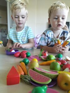 Zdjęcie przedstawia dwóch chłopców bawiących się w kąciku kulinarnym drewnianymi warzywami.
