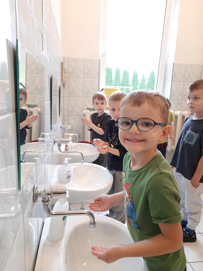 Troje dzieci stoi w łazience przy umywalkach myjąc ręce.