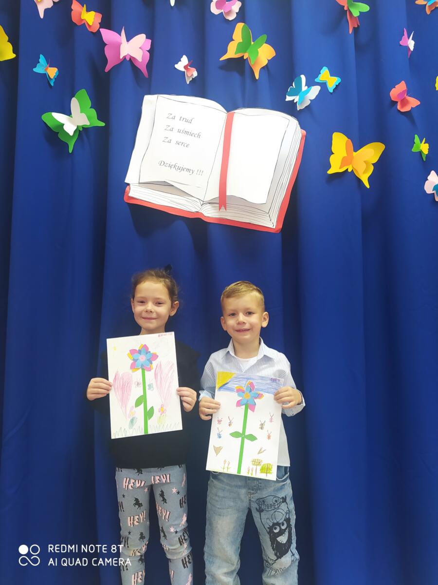Na zdjęciu dwoje dzieci prezentuje wykonane przez siebie laurki - kwiatki dla nauczyciela.