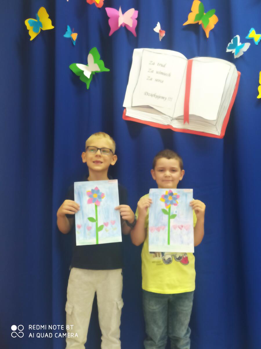 Na zdjęciu dwoje dzieci prezentuje wykonane przez siebie laurki - kwiatki dla nauczyciela.