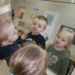 Zdjęcie przedstawia chłopca i dziewczynkę w wieku 3 lat, którzy wykonują ćwiczenia ust i języka przed lustrem