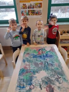 Dzieci prezentują swoją pracę plastyczną ''Kosmos'' wykonaną wspólnie na dużym arkuszu papieru.