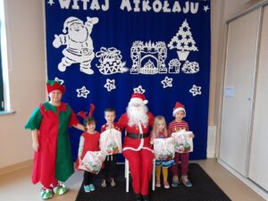 Zdjęcie przedstawia grupę dzieci w mikołajkowych czapkach wraz z Mikołajem i elfem.