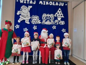 Zdjęcie przedstawia grupę dzieci w mikołajkowych czapkach wraz z Mikołajem i elfem