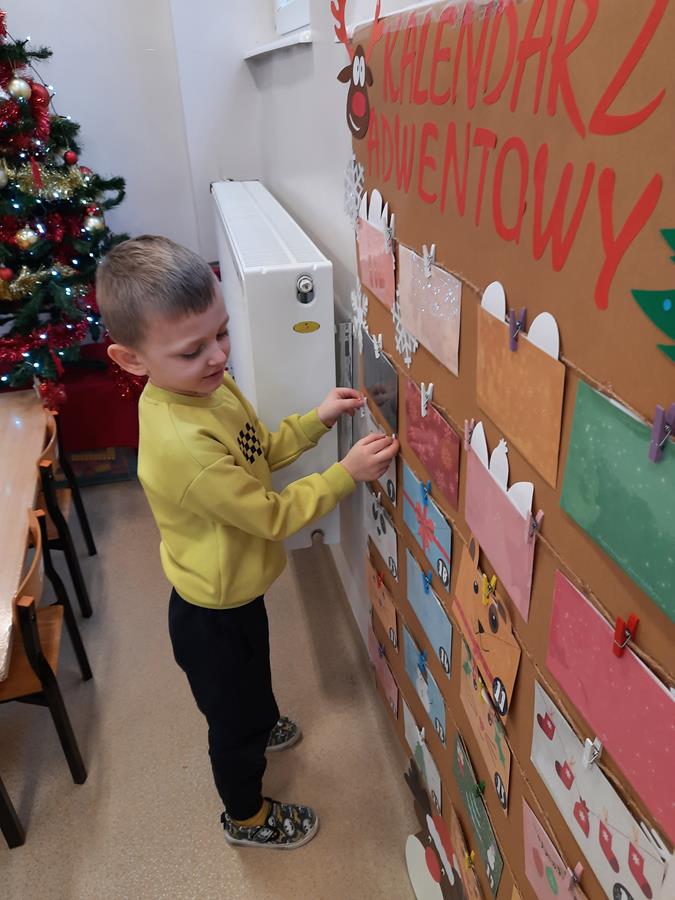 Chłopiec odpina klamerkę na tablicy kalendarza adwentowego.