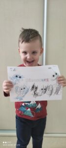 Na zdjęciu widzimy kolejnego chłopca, który prezentuje swoją pracę. Pokolorował na karcie pracy dinozaury..