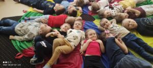 Dzieci leżą na chuście animacyjnej, na wskazanych przez nauczyciela kolorach.