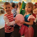 Zdjęcie przedstawia chłopca i dziewczynkę w strojach karnawałowych w tańcu z balonem.