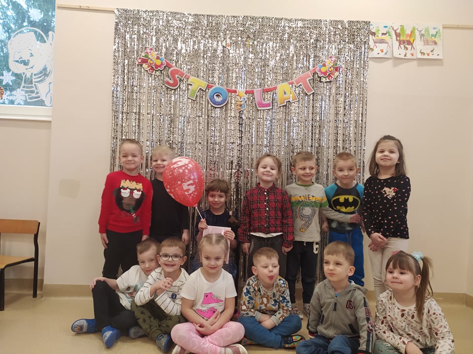 Dzieci pozują do zdjęcia, na środku siedzi dziewczynka z balonem, która obchodzi urodziny.