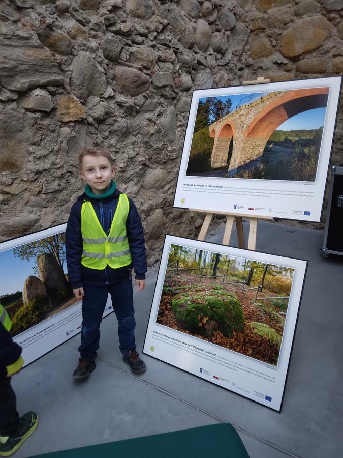 Chłopiec stoi koło fotografii przygotowanej w ramach wystawy fotograficznej.