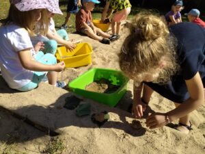 Grupa dzieci zamieniła piaskownicę w kuchnię błotną - mieszają piasek z wodą, ugniatają, klepią...