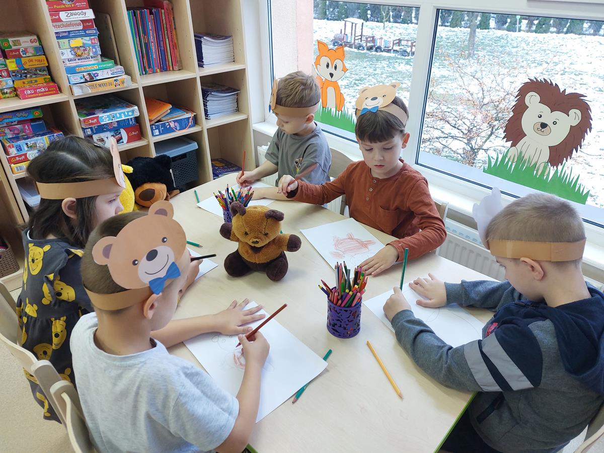 Pięcioro dzieci siedzi przy stoliku, kolorują narysowanego przez siebie misia.