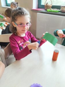 Zdjęcie przedstawia dziewczynkę, która wycina "natkę marchewki" z zielonego papieru.