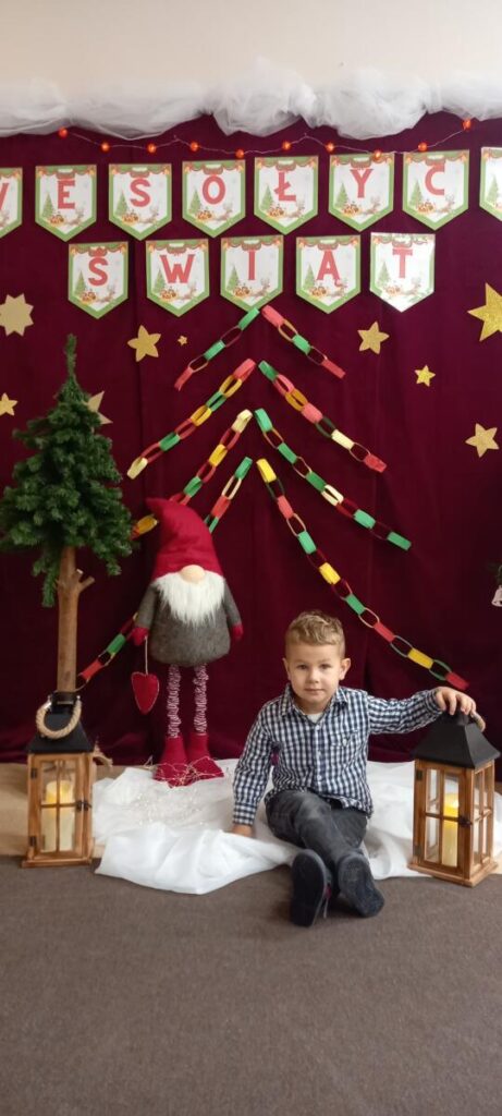 Chłopiec siedzi na tle dekoracji świątecznej i napisu "Wesołych świąt".