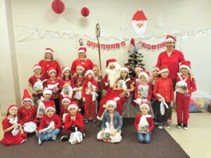 Zdjęcia przedstawia grupę Tygryski,która pozuje do wspólnego zdjęcia z Mikołajem. dzieci ubrane są w mikołajkowe czapki i czerwone bluzki.