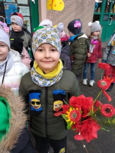 Zdjęcie przedstawia chłopca,który uczestniczy w wiosennym przemarszu połączonym z "Dniem kolorowej skarpetki". Z tej okazji chłopiec ma przyczepione do kurtki skarpetki nie do pary, a w rączce trzyma bukiet kwiatów.