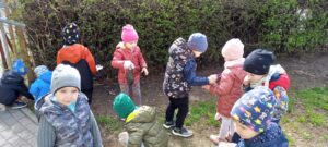 Dzieci zbierają z trawnika odpady za pomocą rękawiczek.