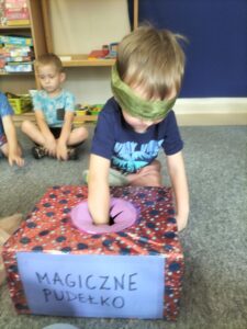 Zdjęcie przedstawia chłopca, który ma zawiązane oczy i losuje przedmiot z "Magicznego pudełka".