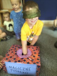 Zdjęcie przedstawia chłopca, który ma zawiązane oczy i losuje przedmiot z "Magicznego pudełka".
