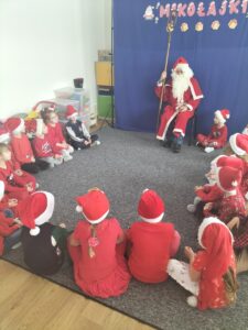 Zdjęcie przedstawia dzieci siedzące w kole, które śpiewają piosenkę dla Świętego Mikołaja.