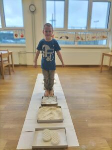 Zdjęcia przedstawia chłopca przez "zimową ścieżkę sensoryczną" złożoną z mąki, ryżu, soli, waty, papierowych kulek, klocków i białej fasoli.