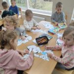 Zdjęcie ukazuje dzieci siedzące przy stole, które kolorują postaci z wybranych baśni i bajek. 