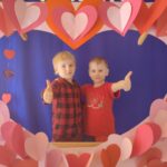Zdjęcie ukazuje dwóch chłopców w fotobudce w kształcie serca.  