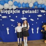 Dziewczyny pozuja do zdjęcia. Stoją przed ścianka ze napisem ' Sięgajcie gwiazd'.