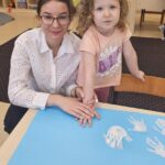 Dziewczynka akceptuje zasady poprzez odciśnięcie swojej rączki pomalowanej białą farbą na brystolu z zasadami.