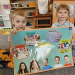 Dwójka dzieci z plakatem prezentującym słownictwo odnośnie gier i zabaw. Dwójka dzieci z plakatem prezentującym słownictwo odnośnie gier i zabaw.