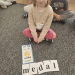 Dziewczynka prezentuje ułożony przez siebie wyraz 'Medal'.