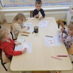 Dzieci siedzą przy stoliku, kolorują kartę pracy, na której jest parasolka.