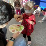 Na zdjeciu widzimy dziecko, które ma przepaskę na oczach. Jej zadaniem jest posmakować warzywo i po smaku powiedzieć jakie to warzywo..