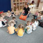 Messenger creation AFEF C D AB BBC Na zdjęciu widzimy panią wraz z dziecmi siedzącymi w okręgu. Pani pokazuje apteczkę i jej zawartość.