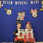 Chłopiec z dziewczynķą pozujący do zdjęcia na ściance. Dzieci przebrane za myszki, trzymają swoją pracę plastyczną.
