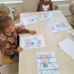 Dzieci układają puzzle przy stoliku. Puzzle - misia.