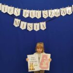 Dziewczynka z dyplomem oraz swoim puzzlowym misiem przyklejonym na kartce.