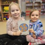 Dwie dziewczynki ukazujące kartę obrazkową z piernikami=ang. Gingerbread.