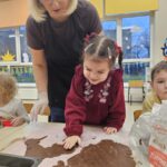 Dziewczynka przy pomocy pani wykrawa foremką pierniczek.