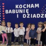 Zdjęcie ukazuje dzieci stojące w rzędzie. Prezentują wierszyk dla babci i dziadka.